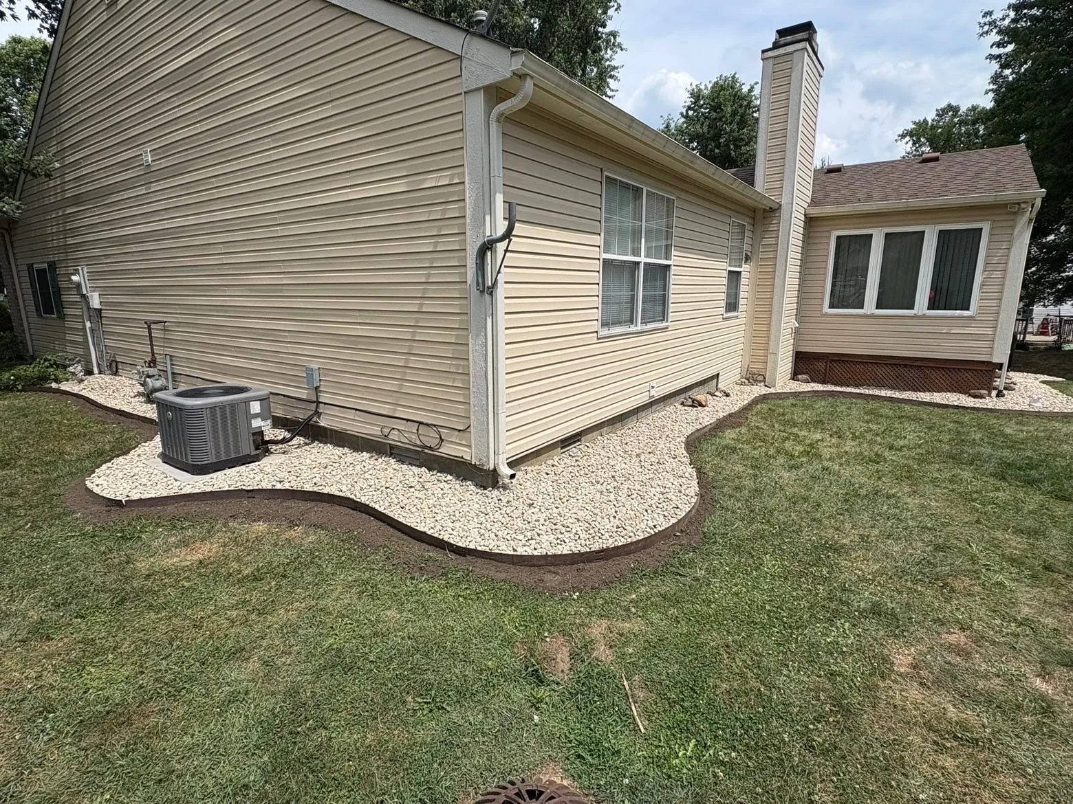 After: the ring gone, a river-rock bed with new edging along the house.